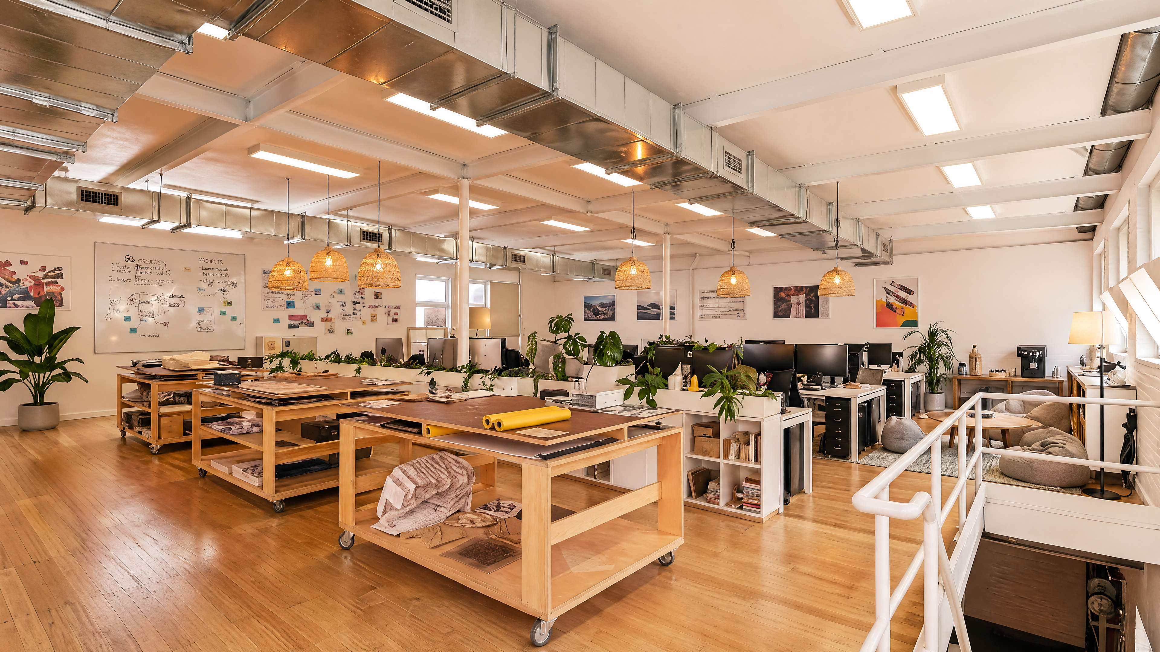 Desks against the windowed wall — work surfaces, monitors, plants.